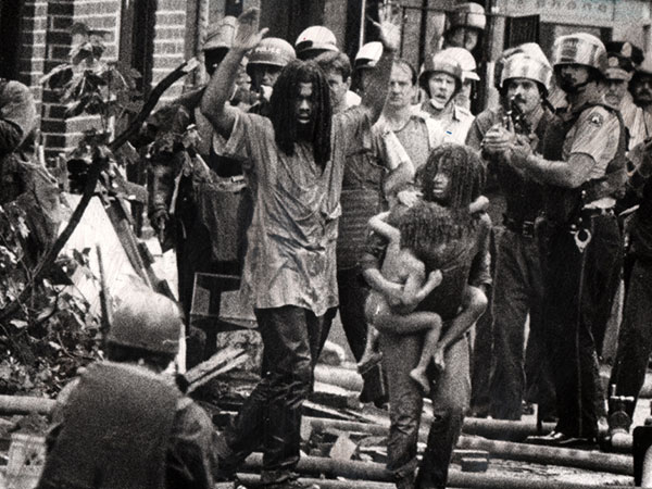 "LET THE FIRE BURN": MOVE members and children emerge from their "headquarters" in a 1978 confrontation. Photo: Sam Psoras / Philadelphia Daily News. 