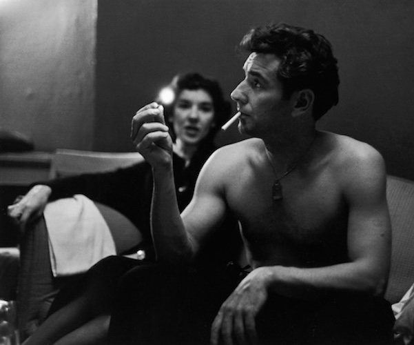 American composer and conductor Leonard Bernstein (1918 - 1990) sits shirtless next to his sister Shirley on a couch and prepares to light a cigarette with a match as she speaks to him, 1940s. (Photo by Ruth Orkin/Getty Images)